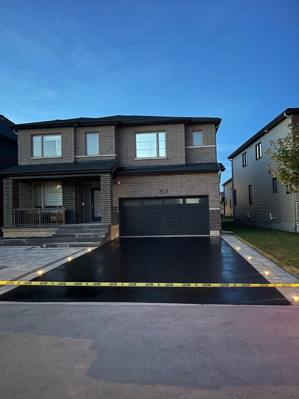 Freshly sealcoated asphalt driveway with interlock border and lights at dusk in Ottawa
