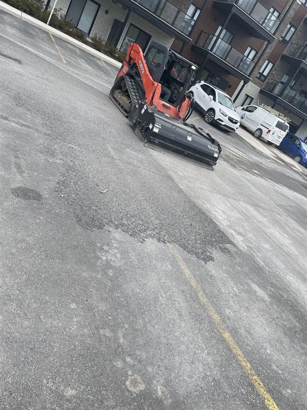 Skid steer with a sweeper attachment cleaning a parking lot before asphalt repair in Ottawa