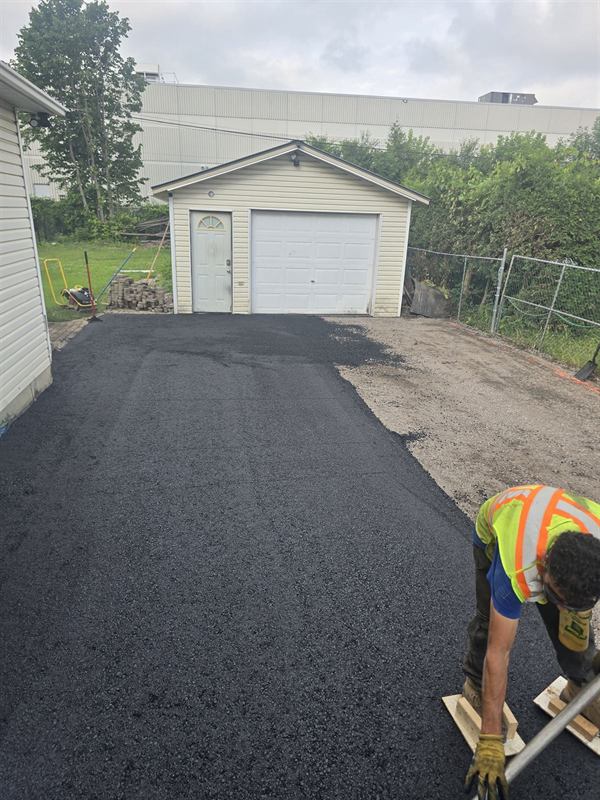 Proseal Plus worker in a high-visibility vest raking fresh asphalt on an Ottawa driveway