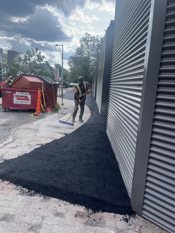 Worker in a high-visibility vest raking hot asphalt on a commercial property in Ottawa
